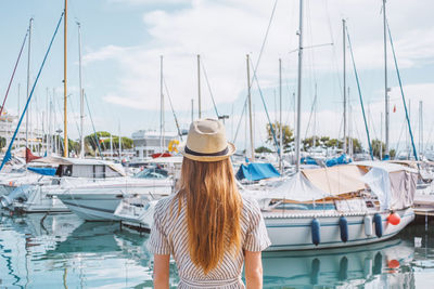 Blonde hair woman in a hat standing with her back on sea, yachts and boats background. nice, france