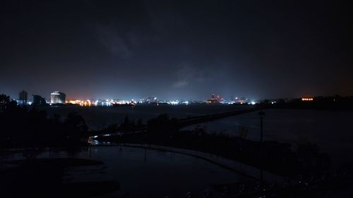 Illuminated city by river against sky at night