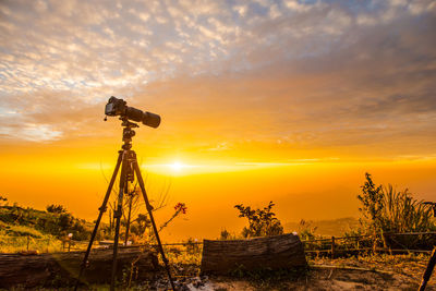 Low angle view of camera on tripod against sky during sunset