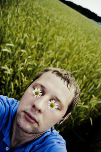 Close-up of man with eyes covered by flowers while listening to music on field