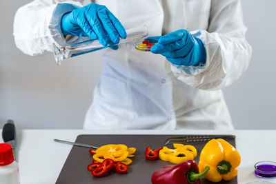 Midsection of scientist experimenting on bell peppers