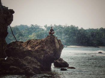 Man sitting on rock against sky