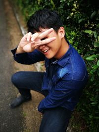 Portrait of smiling teenage boy showing peace sign on footpath