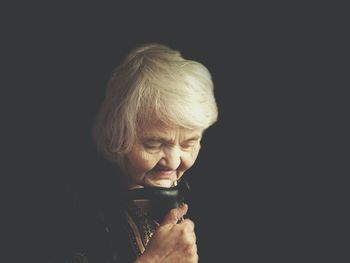 Senior woman holding walking cane against black background