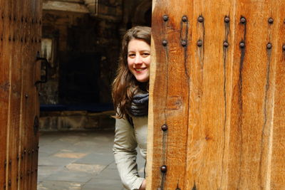 Portrait of smiling young woman standing by wooden door