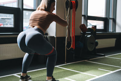 Young brunette woman training muscles with elastic band in fitness club gym