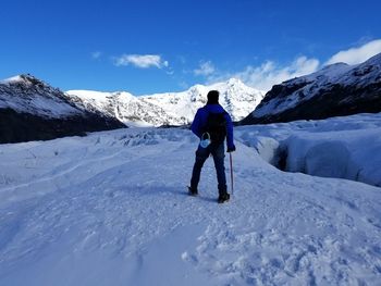 Rear view of man standing on snowcapped mountain against sky