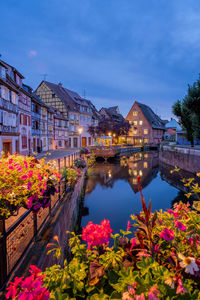 Illuminated building by lake against sky