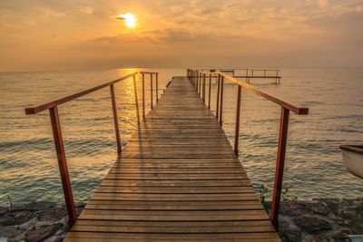 Wooden pier over sea against sky during sunset