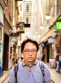 Portrait of young asian man in eyeglasses standing in laneway in the city.