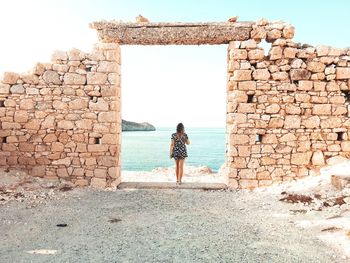 Rear view of woman standing at beach by old entrance