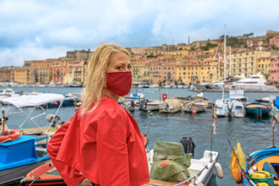 Woman standing by boats in water against sky