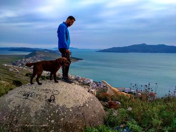 Side view of man standing with dog on rock against sea