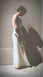 Side view of bride wearing wedding dress while standing by wall