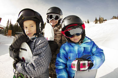 Smiling siblings with snowboards standing on snow covered field