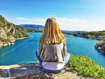 Rear view of girl looking at landscape while sitting on mountain