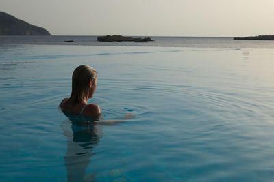 Woman in infinity pool by sea during sunset