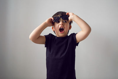 Boy in a black t-shirt stands at home against the background of a white room in sunglasses