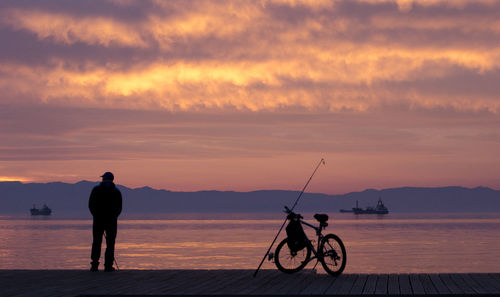 Silhouette man cycling by sea against sky during sunset