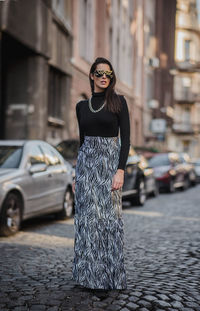 Fashionable woman standing on footpath in city