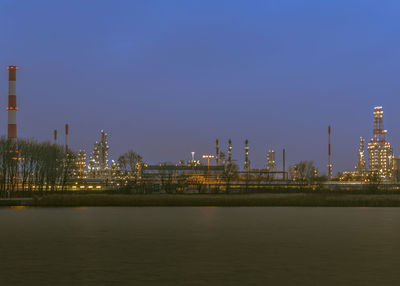 Illuminated city by river against sky at night