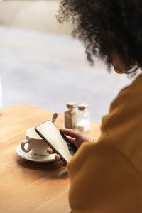 Woman using mobile phone by coffee cup on table