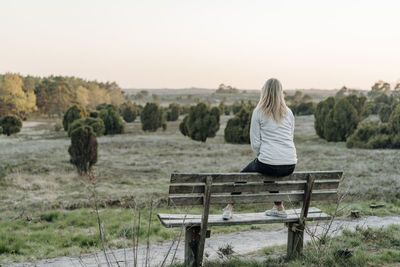 Full length of woman looking at view while sitting on bench during sunset