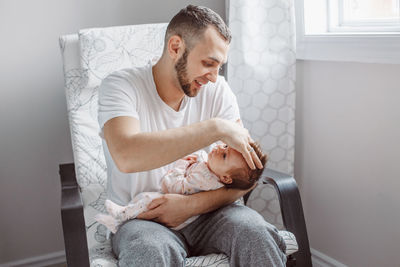 Father with baby girl sitting on chair at home