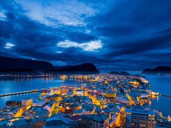 Illuminated cityscape by sea against sky at night