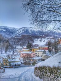 Snow covered houses by trees and mountains against sky