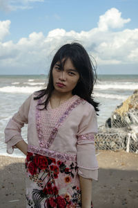 Portrait of woman standing at beach against sky