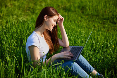 Young woman using laptop while sitting on field