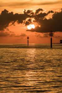 Silhouette lighthouse by sea against sky during sunset