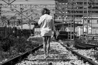 Rear view of woman standing on railroad tracks