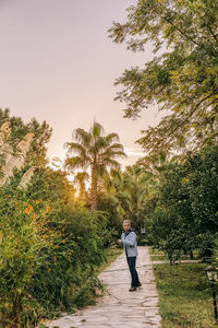 Rear view of woman standing on footpath by palm trees against sky