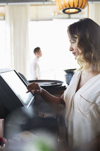 Side view of female owner touching cash register at restaurant