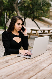 Young woman using mobile phone while sitting on table