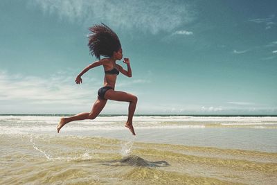 Rear view of woman jumping at beach against sky