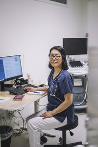 Portrait of smiling female doctor wearing eyeglasses sitting at desk in medical clinic