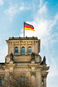 Low angle view of flag on building against cloudy sky