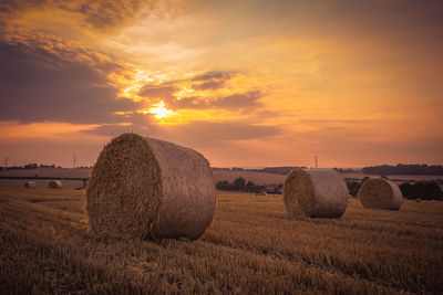 Hay bales on agricultural field against sky during sunset