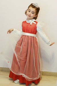 Portrait of smiling girl wearing gown standing against wall