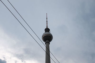 Low angle view of fernsehturm and power cables against sky