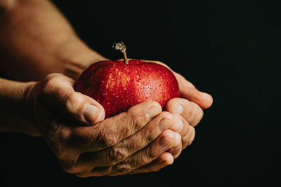 Close-up of hand holding apple over black background
