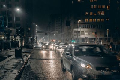 Cars on illuminated street amidst buildings at night