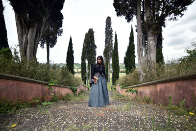 Portrait of woman standing by trees against sky