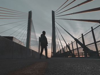 Rear view of man walking on bridge against sky