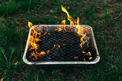 Close-up of coal burning in container on grassy field