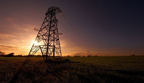 Electricity pylons on field against sky during sunset