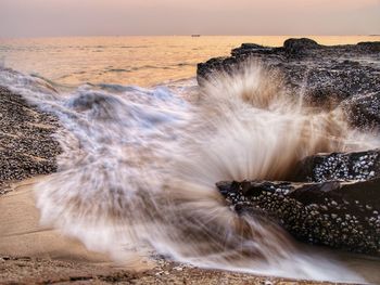 Long exposure image of sea waves splashing on rock against sky